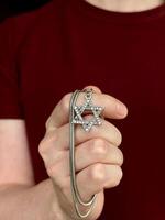 ung män hand innehav en David stjärna magen David nyckel kedja. de stat av israel, judendom, zionism begrepp bild. omvandling till judendom, giyur, påsk. foto