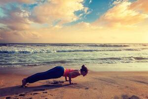 kvinna praxis yoga asana chaturanga dandasana på de strand foto