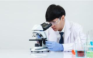 porträtt asiatisk man studerande forskare läkare i skjorta klänning ett person wokk jobb växt ser hand innehav kontrollera mikroskop på vit tabell ser de resultat av vetenskaplig experiment inuti laboratorium foto