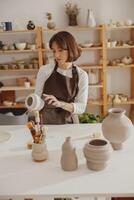 professionell krukmakare bär förkläde innehav oavfyrad lera vas medan stående i krukmakeri studio foto