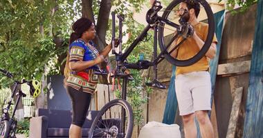 sportälskande man granskning cykel delar i Hem gård medan afrikansk amerikan kvinna cyklist tar bort skadad hjul. par utför cykel underhåll utomhus- med expert- verktyg. tona in skott. foto