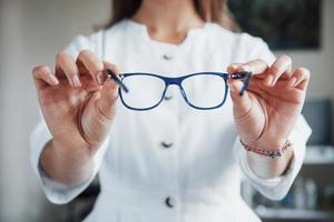 kvinnlig läkare som visar de blå glasögonen genom att hålla den i två händer foto