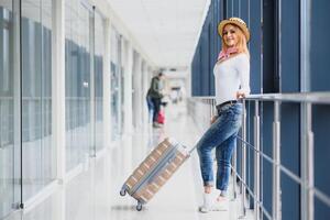 vardagligt klädd ung eleganta kvinna resande kontroll en avgångar styrelse på de flygplats terminal hall i främre av kolla upp i couters. flyg schema visa oskärpa i de bakgrund. fokus på kvinna. foto