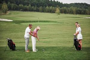 flicka spelar golf och slå av putter på green. hennes lärare hjälper till att utforska tekniken och göra sina första slag foto