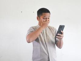 vuxen asiatisk man som visar chockade uttryck när ser till hans telefon foto