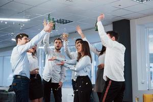 konfetti i luften. foto av ungt lag i klassiska kläder som firar framgång medan de håller drinkar i det moderna bra upplysta kontoret