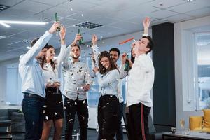 det är så framgång ser ut. foto av ungt lag i klassiska kläder som firar framgång medan de håller drinkar i det moderna bra upplysta kontoret