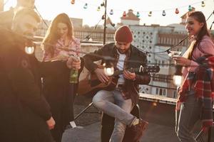 frontvy. gitarr kille med vänner på taket på en solig dag foto