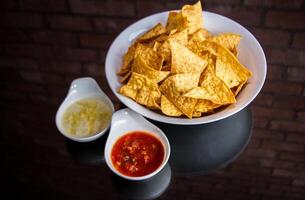 kryddad nachos och salsa med dopp och chili sås eras i en maträtt isolerat på tabell sida se foto