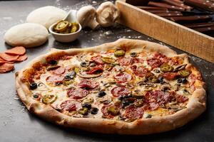 flamin pizza garnering med svamp, pepperoni och oliv isolerat på mörk bakgrund med rå mat topp se av italiensk snabbmat aptitretare foto