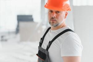 en man med en skägg i en hjälm och arbete kläder. porträtt av en arbetstagare i arbetskläder med kopia Plats. foto