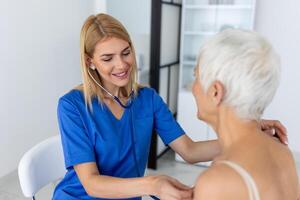 omtänksam kvinna läkare använda sig av phonendoscope undersöka senior patient hjärta Betygsätta på samråd i sjukhus. kvinna sjuksköterska eller gp använda sig av stetoskop lyssna till kvinnas hjärtslag i klinik. foto