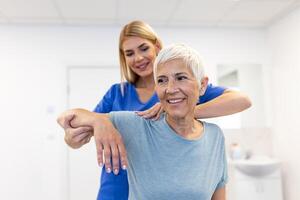 läkare eller fysioterapeut arbetssätt granskning behandla skadade ärm av senior kvinna patient, stretching och träning, håller på med de rehabilitering terapi smärta i klinik. foto