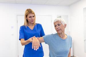 läkare eller fysioterapeut arbetssätt granskning behandla skadade ärm av senior kvinna patient, stretching och träning, håller på med de rehabilitering terapi smärta i klinik. foto