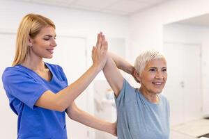 läkare eller fysioterapeut arbetssätt granskning behandla skadade ärm av senior kvinna patient, stretching och träning, håller på med de rehabilitering terapi smärta i klinik. foto