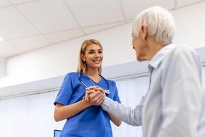 läkare ger hoppas. stänga upp skott av ung kvinna läkare lutande framåt- till leende äldre lady patient innehav henne hand i handflatorna. kvinna vaktmästare i vit täcka stödjande uppmuntrande gammal person foto