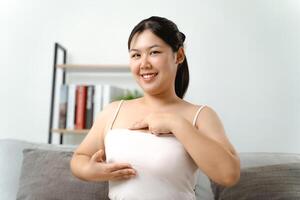 asiatisk kvinna kontroll klumpar på henne bröst för tecken av bröst cancer förbi henne själv på Hem. foto