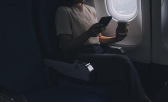 asiatisk kvinna njuter åtnjuter en kaffe bekväm flyg medan Sammanträde i de flygplan stuga, passagerare nära de fönster. foto