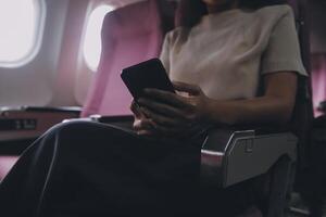 asiatisk kvinna passagerare Sammanträde i flygplan nära fönster och läsning Nyheter från social nät eller använder sig av resa tillämpningar i smartphone foto