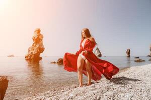 kvinna resa hav. Lycklig turist i röd klänning njut av tar bild utomhus för minnen. kvinna resande Framställ på de sten på hav bukt omgiven förbi vulkanisk berg, delning resa äventyr resa foto