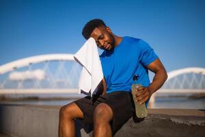 porträtt av trött ung afrikan-amerikan man vem våtservetter de svettas från hans ansikte efter joggning. foto