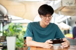 en man sitter på en tabell utomhus, ser på hans smartphone, spelar en mobil spel eller tittar på en foto