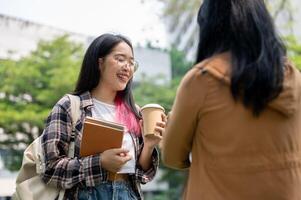 en glad ung asiatisk kvinna högskola studerande njut av talande till henne vän på de campus parkera. foto