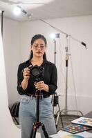 en professionell asiatisk kvinna fotograf är justeras henne dslr kamera på en stativ stå. foto