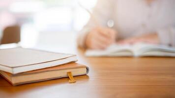 böcker på en trä- tabell med en kvinna skrivning i en bok eller håller på med läxa i de bakgrund. foto