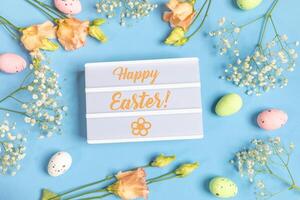 inskrift Lycklig påsk omgiven förbi dekorativ ägg, vit och persika blommor på blå. topp se. foto