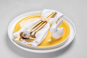 gul vit tallrikar, vit servett, guld bestick och vaktel ägg, keramisk kanin på dem. påsk tabell. foto