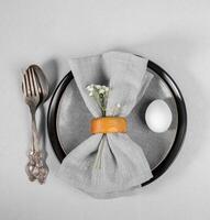 påsk tjänande i grå toner. eleganta tallrikar, servett, vit ägg, årgång bestick, blomma. topp se. foto