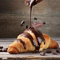 choklad faller på croissant färsk bakad på trä- tabell foto