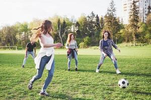 en grupp vänner i ledig outfit spelar fotboll utomhus. folk har kul och har kul. aktiv vila och vacker solnedgång foto