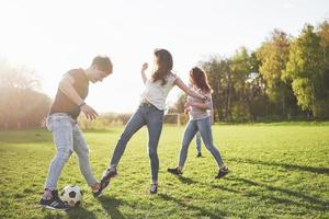 en grupp vänner i ledig outfit spelar fotboll utomhus. folk har kul och har kul. aktiv vila och vacker solnedgång foto