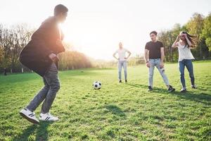 en grupp vänner i ledig outfit spelar fotboll utomhus. folk har kul och har kul. aktiv vila och vacker solnedgång foto