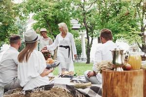 kvinnor går till bordet. grupp av vuxna vänner har en vila och konversation på bakgården av restaurang vid middagstid foto