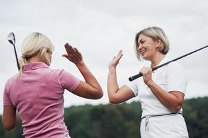 två kvinnliga golfspelare ger high five i bakgrunden av vackra gröna skogar foto