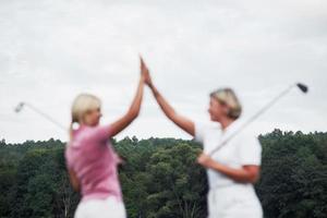 fokuserat foto på baksidan. två kvinnliga golfspelare ger high five i bakgrunden av vackra gröna skogar