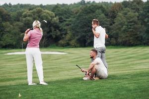 tittar på bollen. tre vänner spenderar god tid på planen och spelar golf och tittar på skottet foto