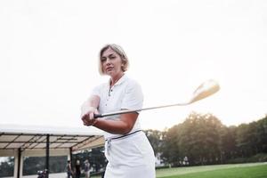 foto av vacker blond vuxen kvinna som håller golfpinne på det gröna sportfältet