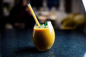 mango morot äpple smoothie i en glas på mörk bakgrund med glas sugrör foto