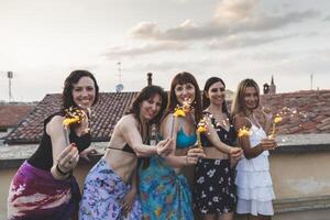 grupp av Lycklig kvinna vänner innehav sparklers på taket fest foto