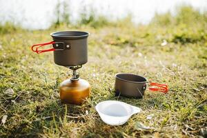 en uppsättning av maträtter för en turist på en vandra, kompakt Utrustning, en små volym av en kopp, en turist brännare, en pott för äter, ett aluminium legering, camping i de skog. foto