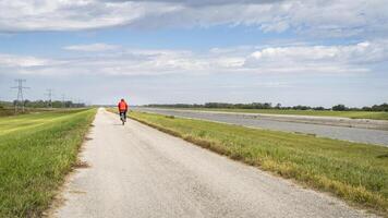 ensam cyklist är ridning en grus touring cykel - cykling på en levee spår längs kedja av stenar kanal nära granit stad i Illinois foto