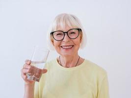 senior kvinna med glas vatten och dricksvatten. hälsosam livsstil, sport, anti-age koncept foto