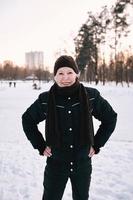 senior kvinna i hatt och sportig jacka jogging i snö vinter park. vinter, ålder, sport, aktivitet, säsongskoncept foto