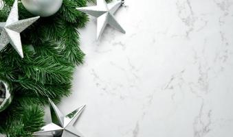 gröna tallblad på vit marmorbakgrund, juldekorationer i ljus silverfärg. enkelt och kreativt julkoncept. foto
