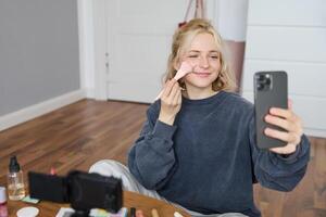 porträtt av ung kvinna, flicka skönhet bloggare, inspelning vlog i henne sovrum, håller på med smink handledning för social media följare, tar selfies, leva strömning på mobil telefon app foto