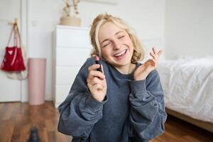 porträtt av leende skön kvinna i henne rum, Sammanträde och som visar läppstift, rekommenderar favorit skönhet produkt, innehåll tillverkare inspelning en av själv för social media blog foto